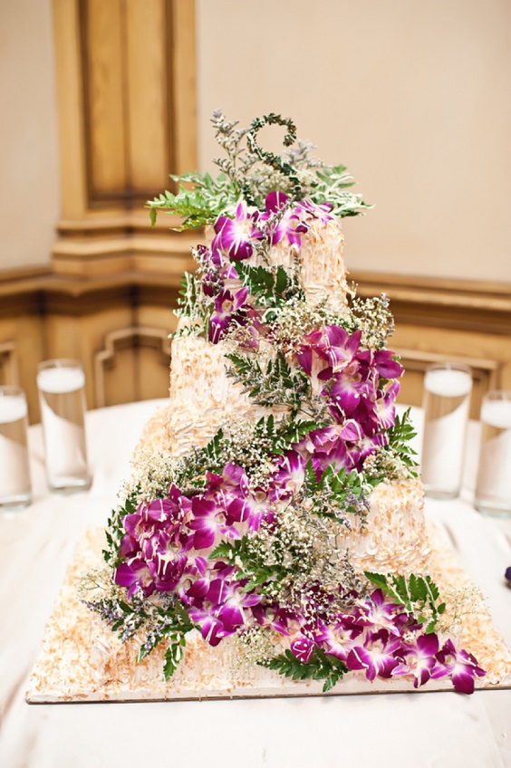 champagne wedding cake dotted with purple flowers and greenery for february wedding colors 2022 champagne purple and black colors