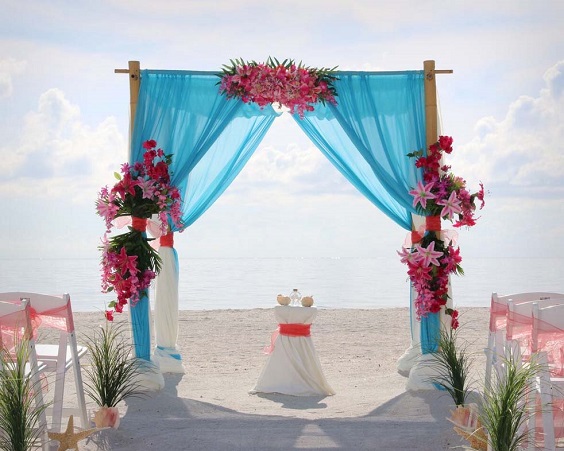 wedding arch with turquoise cloth fuschia flowers for sping wedding colors 2022 fuschia turquoise gold colors