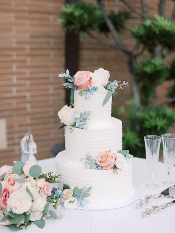 white wedding cake dotted with blush pink and white flowers and greenery for fall wedding colors 2023 dusty blue and blush pink
