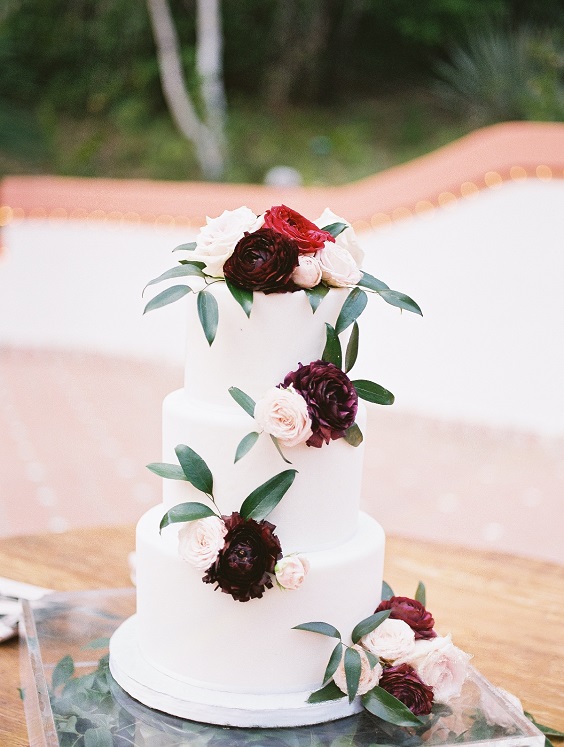 white wedding cake dotted with burgundy flower and greenery for sage green wedding colors 2023 sage green and burgundy