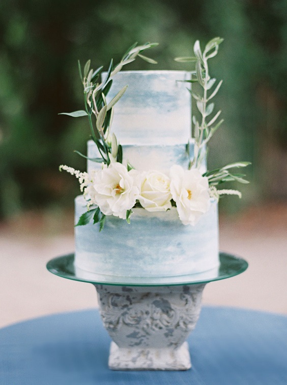 white and dusty blue wedding cake dotted with greenery and white flower for sage green wedding colors 2023 sage green and dusty blue