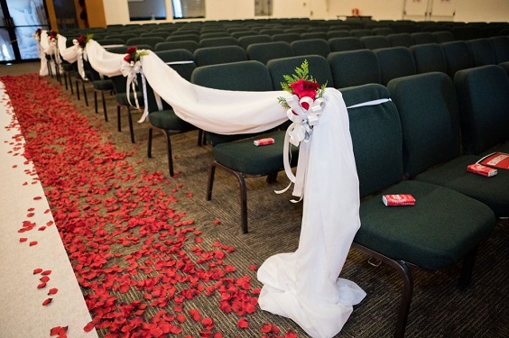 wedding aisle with red rose petals wedding chairs decorated with white sash red flower and green pine for red wedding colors 2023 red and green