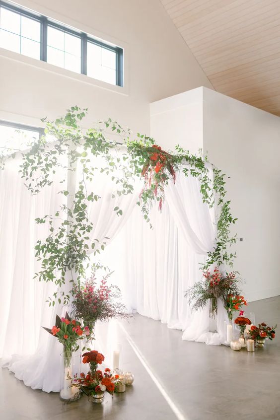 wedding arch decorated with white cloth red flowers greenery and gold candle holders for red wedding colors 2023 red gold and white