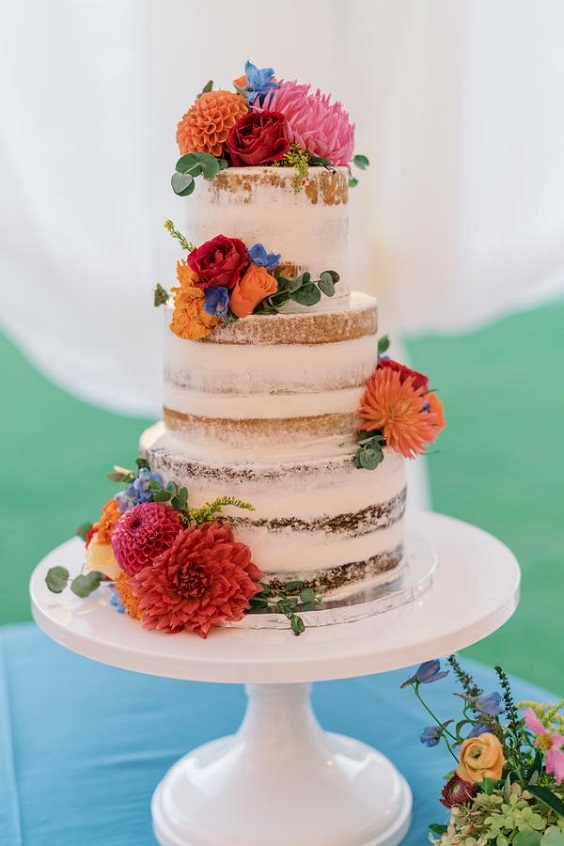 nude wedding cake dotted with orange pink blue flowers and greenery for august wedding colors 2023 rich colors