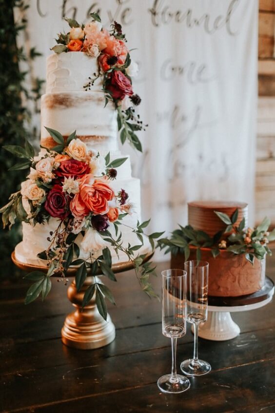 white wedding cake dotted with rust terro cotta flowers and greenery for november wedding colors 2023 rust and terro cotta