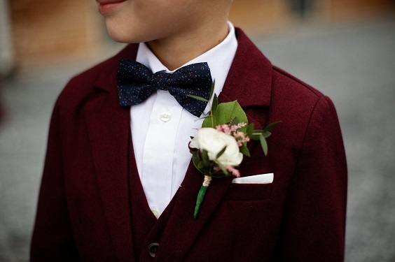 junior groomsmen in maroon suit and greenery and white flower corsage for november wedding colors 2023 maroon and green