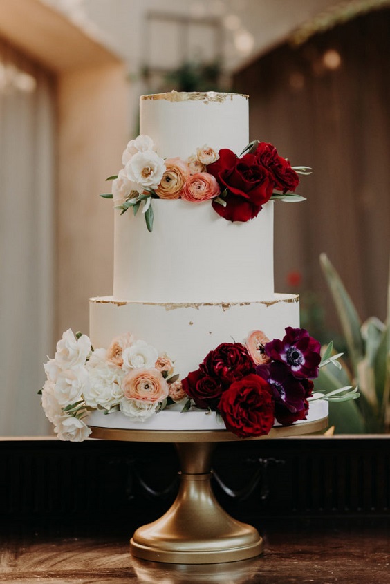 white wedding cake dotted with maroon flowers for november wedding colors 2023 maroon and green