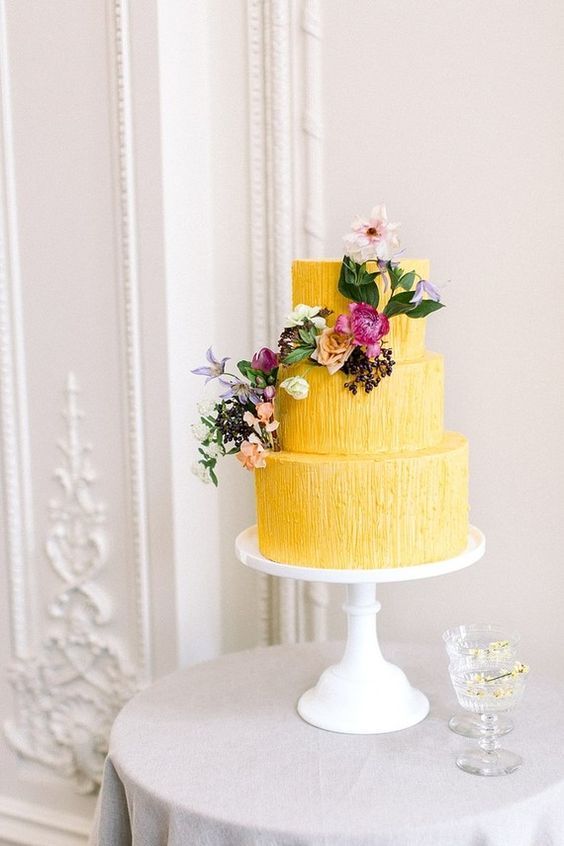 mustard yellow wedding cake dotted with lavender pink flowers and greenery for november wedding colors 2023 mustard yellow and lavender