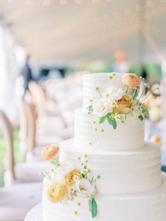 white wedding cake dotted with pale yellow flower decoration for april wedding color schemes for 2023 blush dusty blue and pale yellow