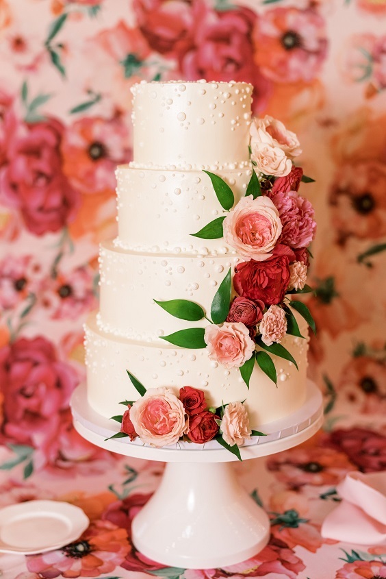 white wedding cake dotted with red and pink flowers for april wedding color schemes for 2023 shades of pink and red