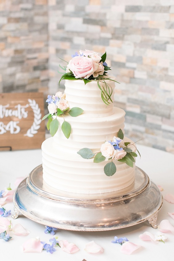 white wedding cake dotted with blush pink dusty blue flower and green leaves for dusty blue wedding themes for 2023 dusty blue and blush pink