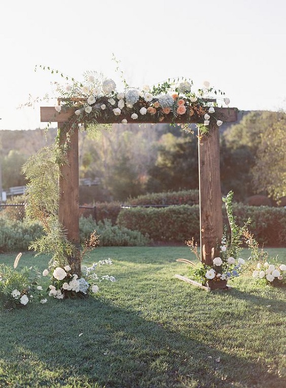 wood wedding arch decorated with white coral and peach flowers for dusty blue wedding themes for 2023 dusty blue coral and peach