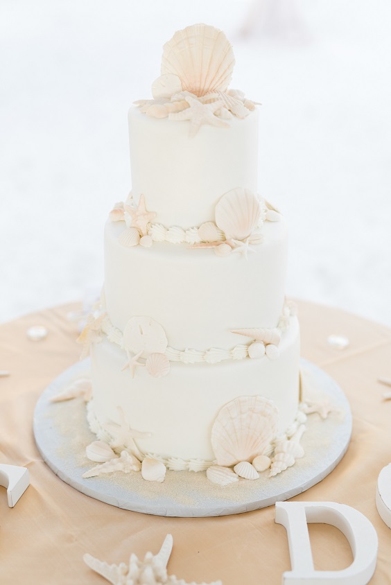 white wedding cake dotted with shells for great summer wedding color palettes for 2024 mauve and champagne