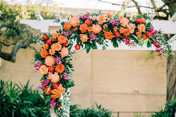 wedding arch decorated with fuschia and orange flowers and greenery for great summer wedding color palettes for 2024 sage orange and fuschia