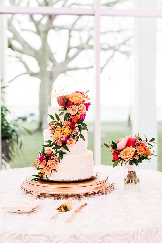 wedding cake dotted with fuschia and orange flowers and greenery for great summer wedding color palettes for 2024 sage orange and fuschia