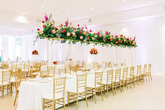 wedding hall with hanging fuschia and orange flowers ceiling for great summer wedding color palettes for 2024 sage orange and fuschia