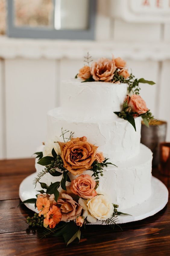white wedding cake dotted with burnt orange flower for emerald green wedding color schemes for 2024 emerald green and burnt orange
