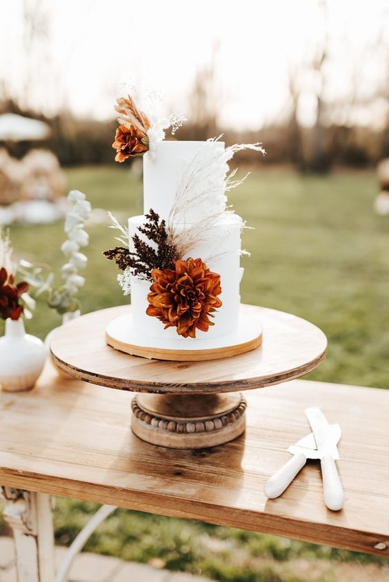 white wedding cake dotted with beige and burnt orange flowers for destination wedding colors 2024 terracotta and beige