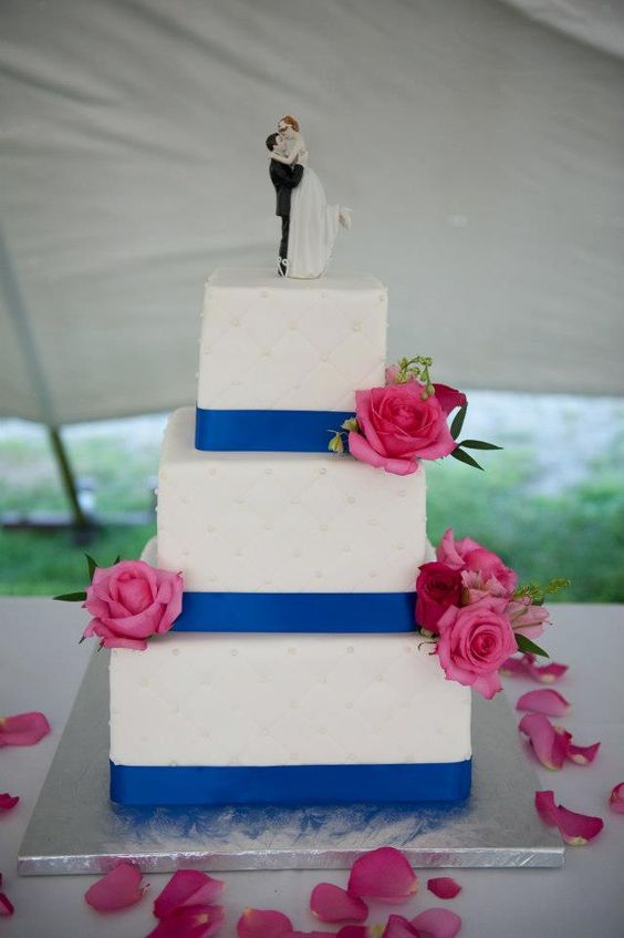 white wedding cake dotted with royal blue ribbons and fuschia flowers for royal blue wedding colors 2024 royal blue and fuschia
