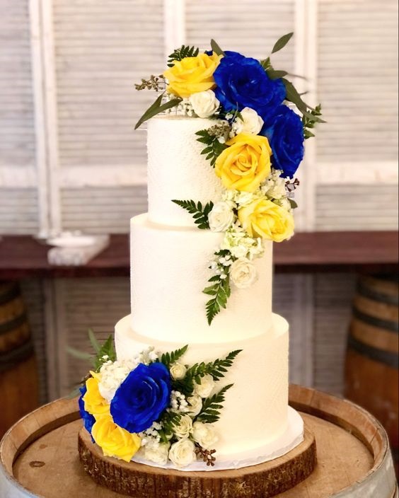 white wedding cake dotted with yellow and royal blue flowers and greenery for royal blue wedding colors 2024 royal blue and yellow