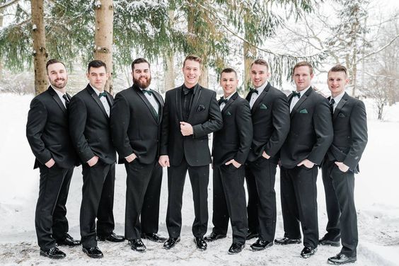 black groomsmen suits emerald green ties bowties and corsages for december wedding colors 2024 emerald green black and gold