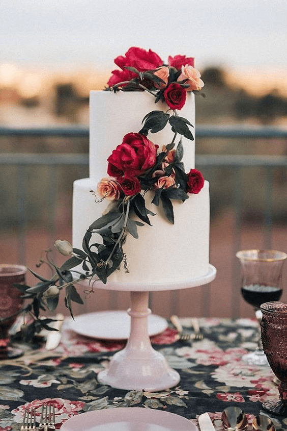 white wedding cake with red flowers and green greenery for march wedding colors combos for 2024 burgundy and dark red