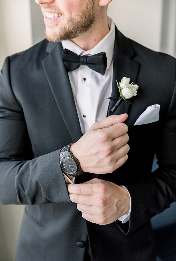 black bridegroom suit with black tie and white flower boutonniere for january wedding colors for 2024 black white and greenery