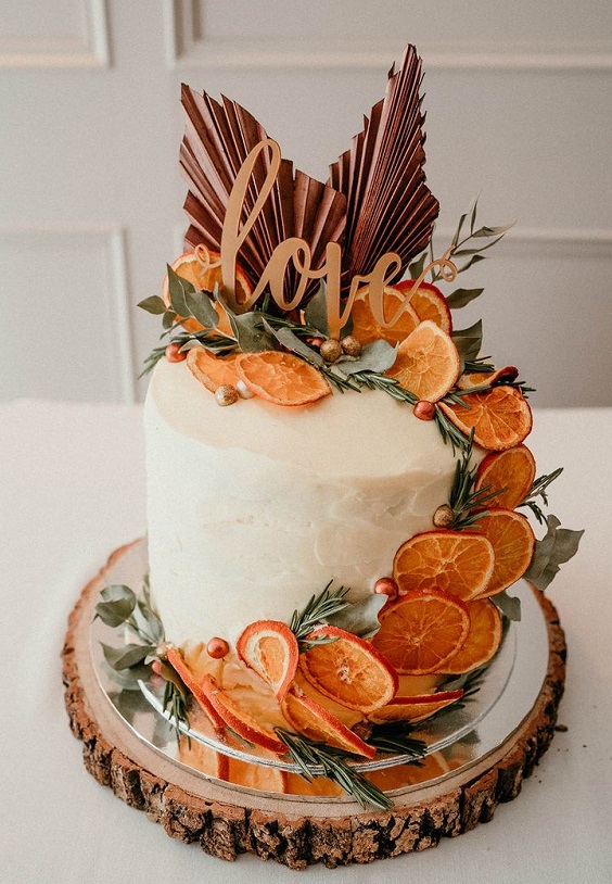 white wedding cake dotted with burnt orange dried orange slices and olive green leaves for burnt orange wedding colors for 2024 burnt orange and olive green