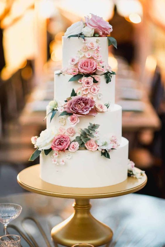 white wedding cake with dusty rose flowers in gold wedding stand for emerald green and gold wedding colors emerald gold and dusty rose