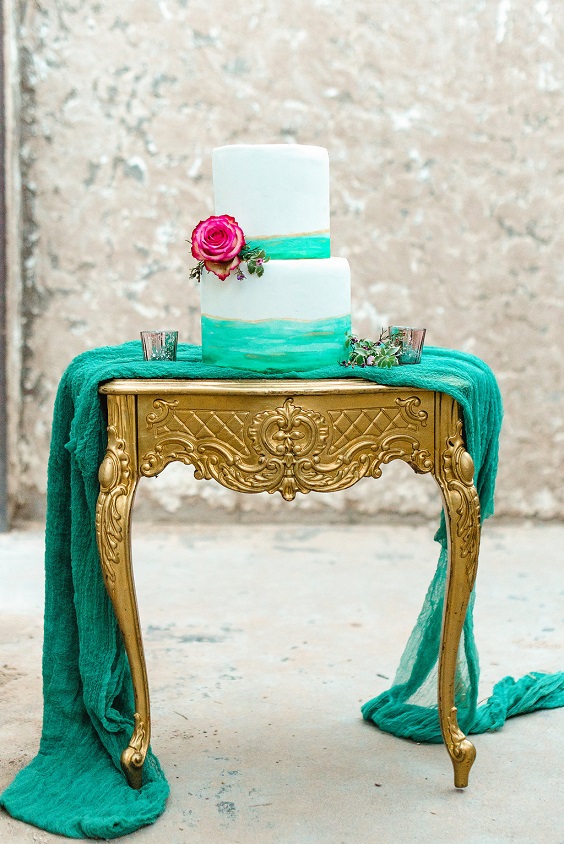 wedding cake dotted with fuschia flowers on gold table for emerald green and gold wedding colors emerald gold and fuschia