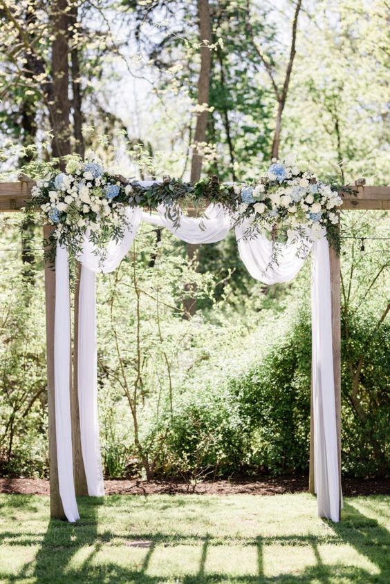 white wedding arch with conflower blue and ivory flowers for july wedding colors combos for 2024 conflower blue and ivory