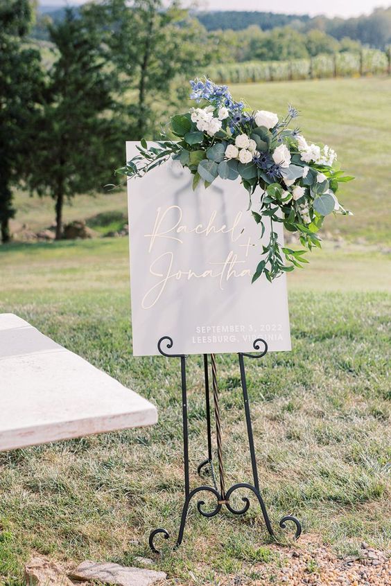 white welcome sign with conflower blue and ivory flowers for july wedding colors combos for 2024 conflower blue and ivory