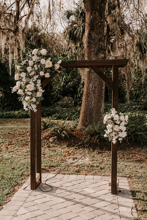 wooden wedding ceremony arch with white flowers and greenery for rustic themed wedding colors for 2025 sage green and slate blue