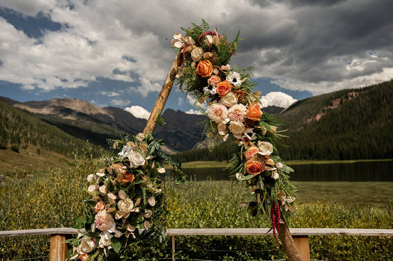 wooden triangle ceremony arch with terracotta and orange flowers and greenery for rustic themed wedding colors for 2025 terracotta and orange