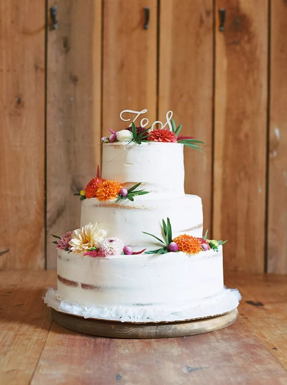 white wedding cake dotted with red and orange flowers for navy blue wedding colors for 2025 navy blue red orange