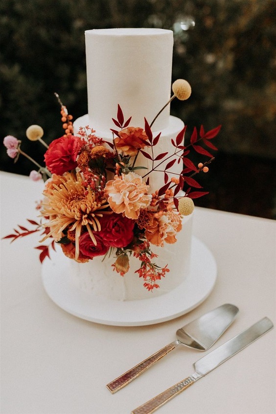 white wedding cake dotted with burgundy and burnt orange flowers for burgundy wedding colors for 2025 burgundy and burnt orange